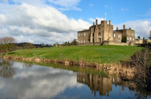 Ripley Castle reflected in a pond and green landscaping